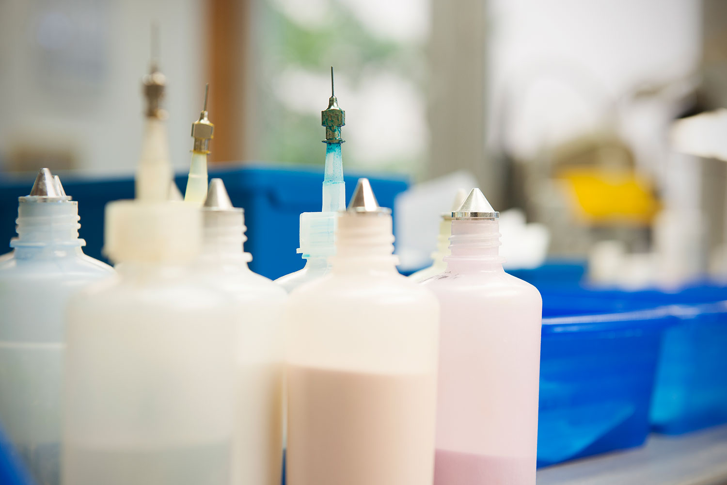 Das Bild zeigt mehrere weiße Flaschen, die mit Farbe gefüllt sind und die zum Einfärben von Zahnspangen im zahntechnischen Labor der Kieferothopaediepraxis Dr. Susanne Guentzer in Trier verwendet werden
