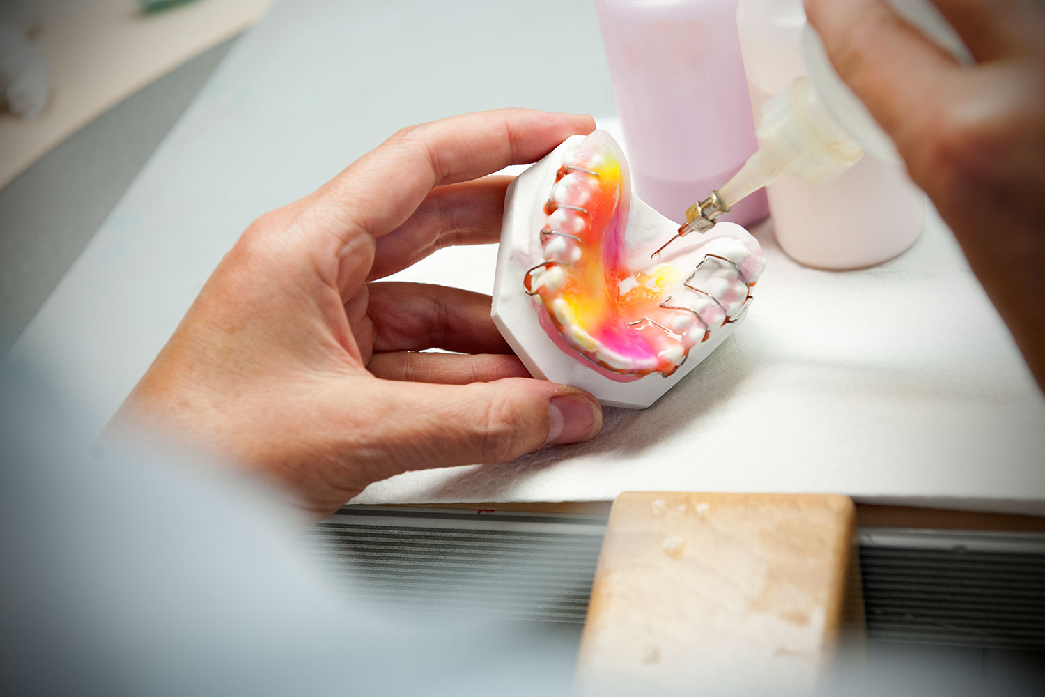 Das Bild zeigt, wie bei der Herstellung einer Zahnspange mit einer Flasche Farbe hinzugefügt wird um die Zahnspange bunt einzufärben.